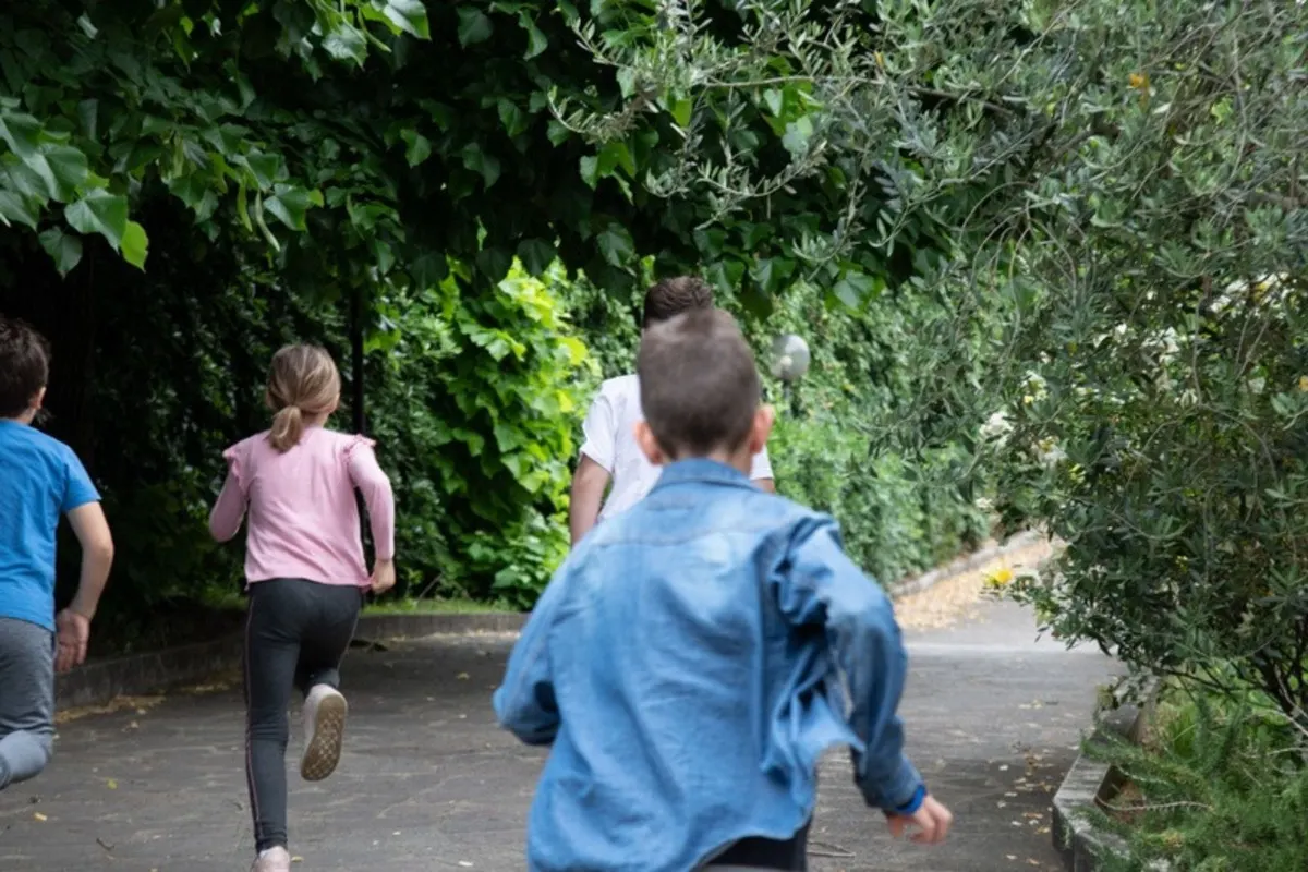 Bambini che corrono lungo un viale alberato nel verde del quartiere