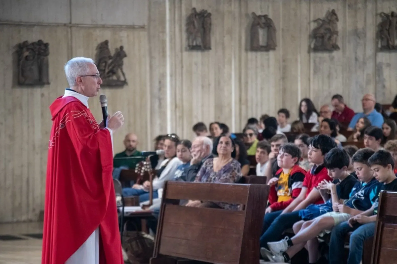 Un sacerdote in casula rossa parla ai fedeli e ai ragazzi durante la Messa a Santa Maria del Carmelo